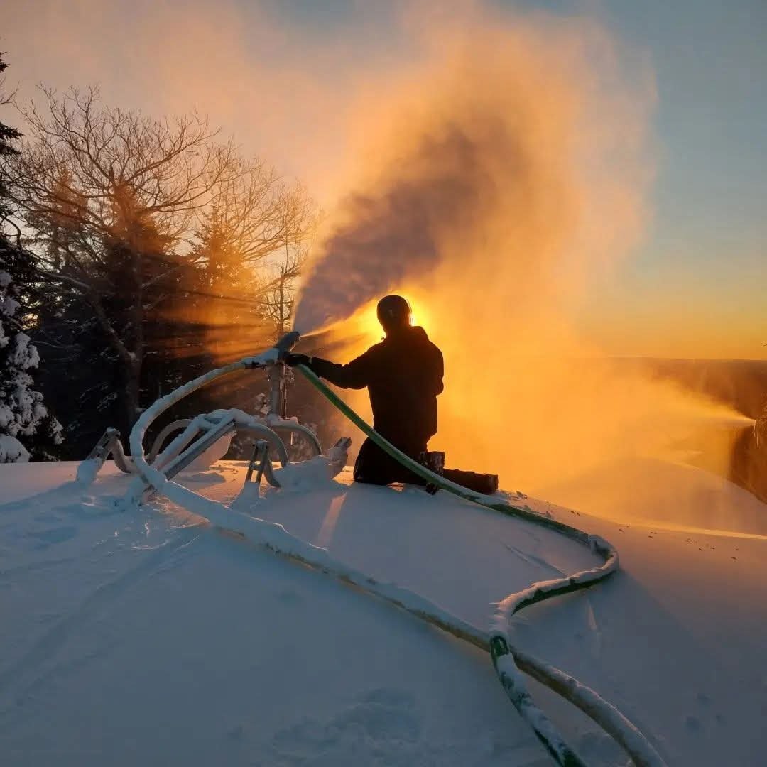 Sean making snow on the mountain at sunrise, backlit by the sun